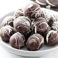 A white dessert stand with a stack of Oreo Truffles on top and Oreo Cookies in the background.
