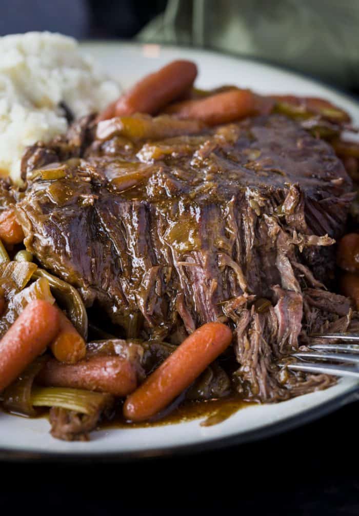 This Mississippi Pot Roast simmers slowly in your crock pot with just 4 other ingredients to create the perfect balance of savory flavors. Tender Crock Pot Mississippi Pot Roast with baby carrots on a white plate.