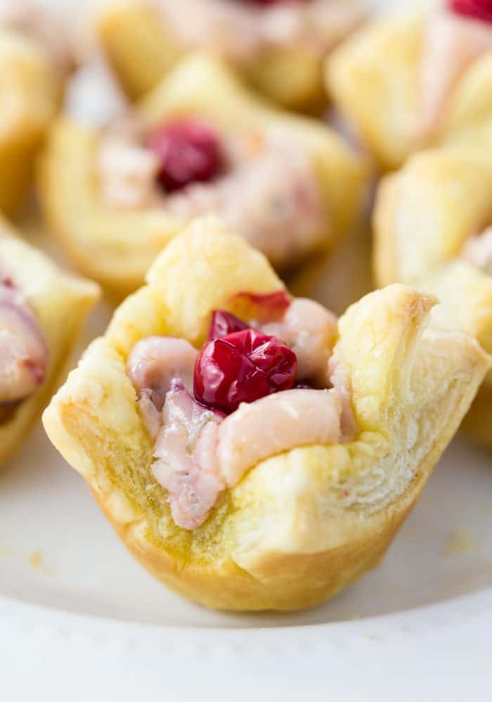 These sweet cranberry tartlets are a perfect holiday snack idea that family and friends will love. The perfect finger food for a crowd! #appetizerideas #easyrecipes #dessert #holidaydessertideas #thanksgivingdessert #christmasdessert Cream Cheese Cranberry Tartlets topped with fresh cranberries on a white surface.