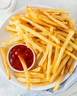 A white plate full of homemade McDonald's French Fries and kechup.