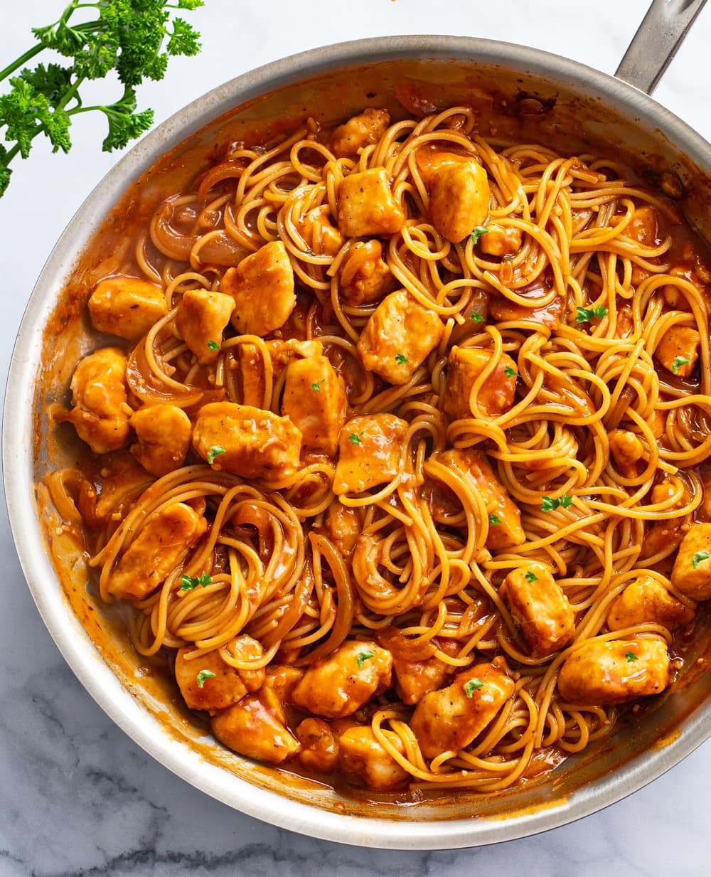Chicken Scallopini in a skillet with red sauce, spaghetti, and chicken.