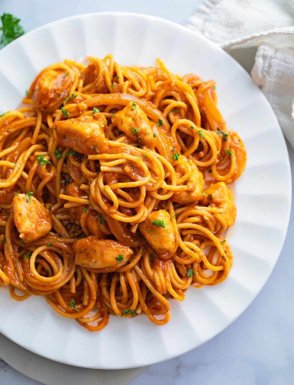 Chicken Scallopini Pasta on a white plate with red sauce and parsley on top.