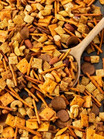 A baking sheet with spicy chex mix with a wooden spoon.