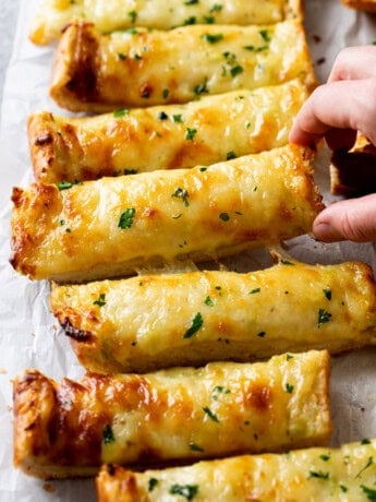 A hand picking up Garlic Bread with Cheese.