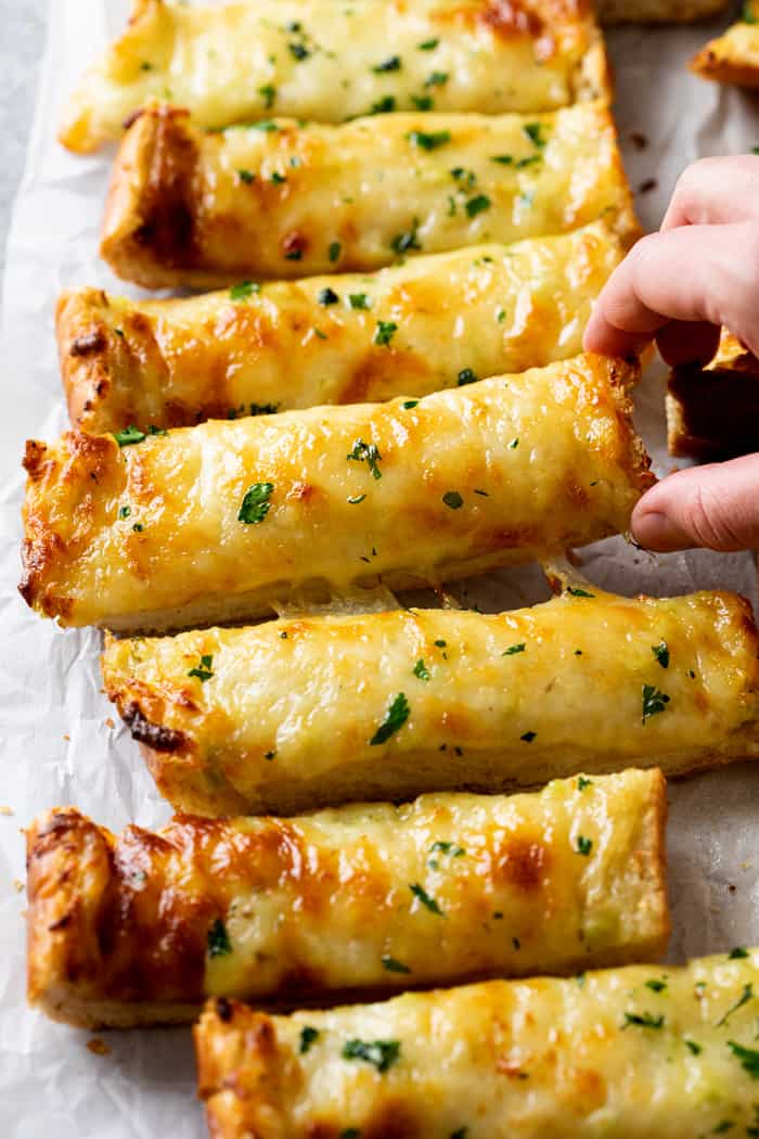 A hand picking up Garlic Bread with Cheese.