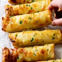 A hand pulling up a slice of Garlic Bread with Cheese from a line of them.