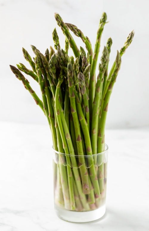 A glass of water with asparagus in it to keep it fresh.