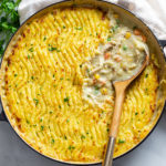 A skillet filled with Chicken Shepherd's Pie with a wooden spoon scooping up the filling.
