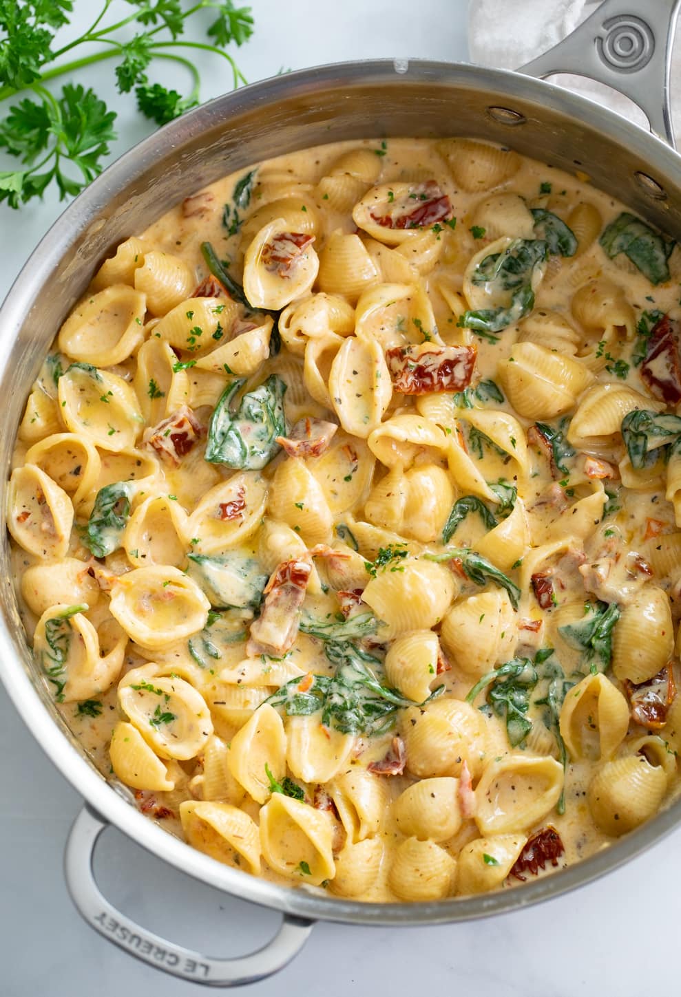 A skillet filled with creamy Tuscan Mac and Cheese with spinach and sundried tomatoes.