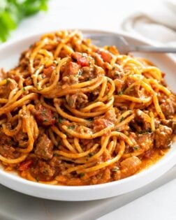 A white plate with Taco Spaghetti with taco meat and diced tomatoes.