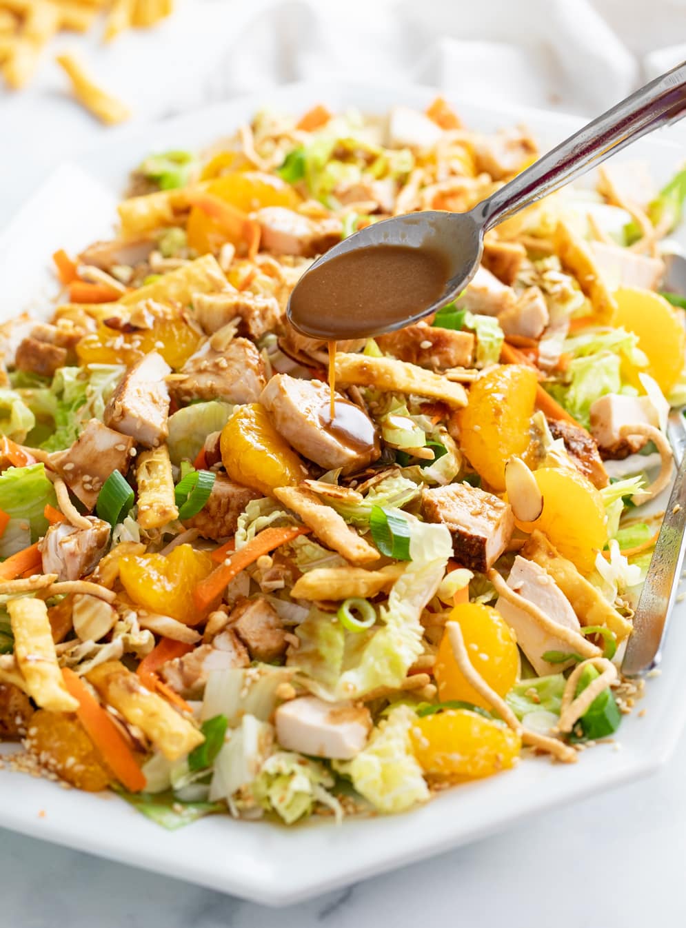 A spoon drizzling salad dressing over Chinese Chicken Salad.