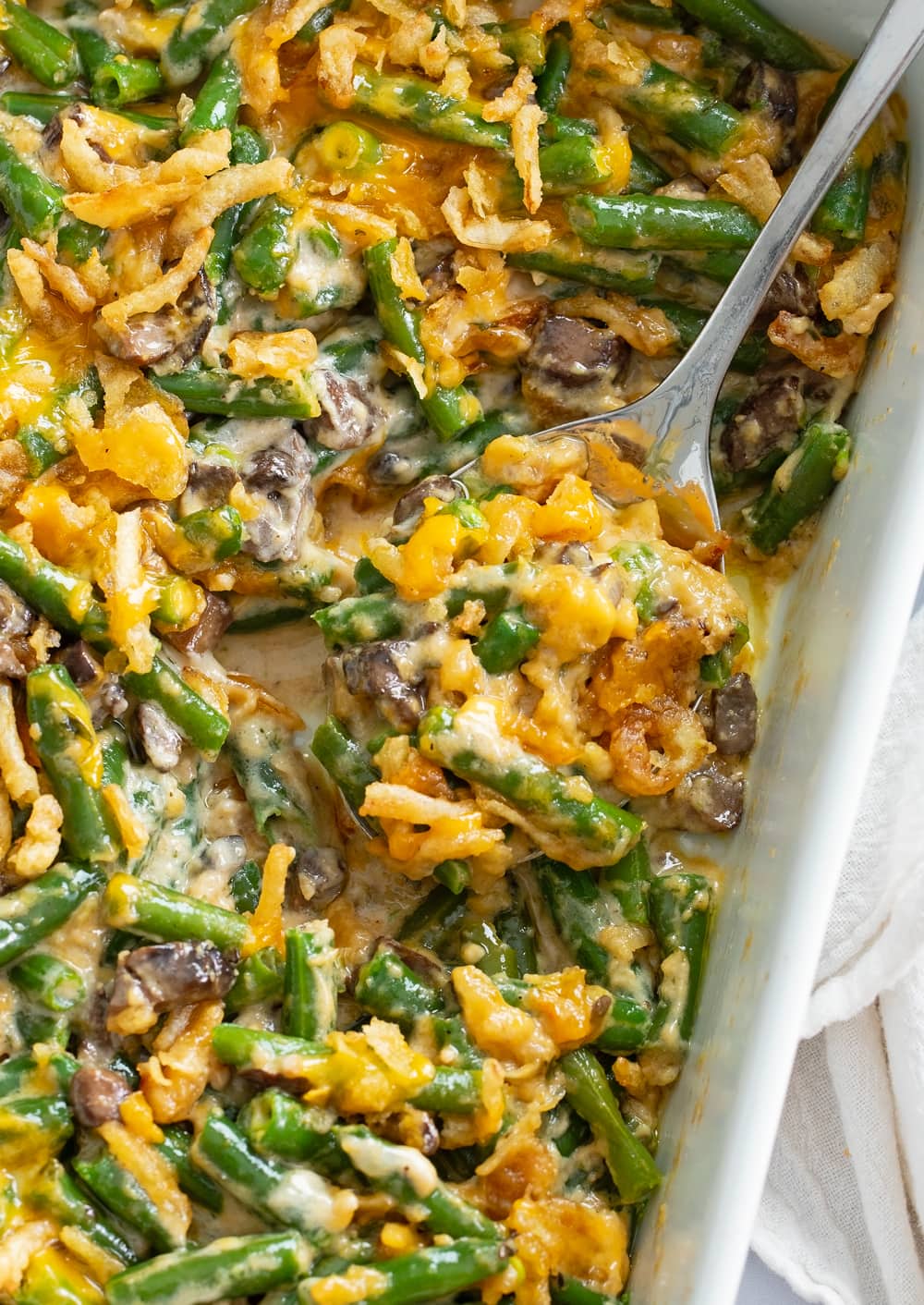 A spoon filled with Green Bean Casserole from a casserole dish.