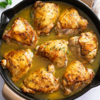 A skillet filled with Baked Chicken Thighs in sauce with fresh thyme on top.