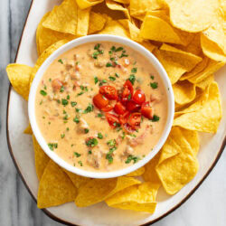 Rotel Dip in a white bowl on a platter with tortilla chips.