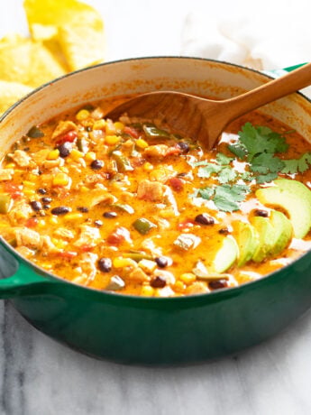 Chicken Poblano Soup in a green Dutch oven with sliced avocado on top and a spoon on the back.