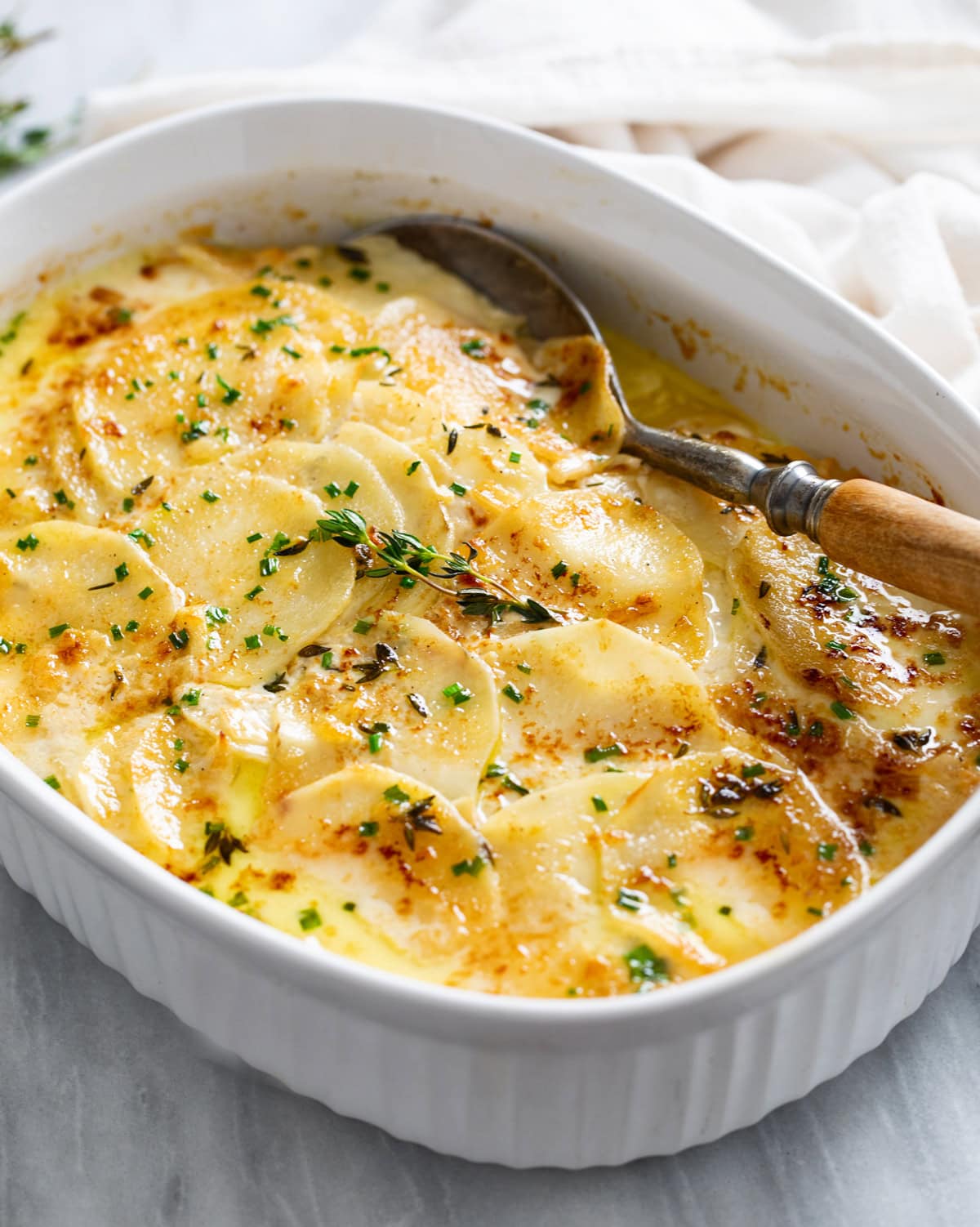 Side view of Au Gratin Potatoes in a baking dish with a serving spoon on the side.