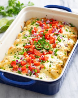 White Chicken Enchiladas in a baking dished topped with diced tomatoes, green and red onions, cilantro, and jalapenos.
