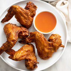 Fried Chinese Chicken Wings on a white plate with sweet and sour sauce on the side.