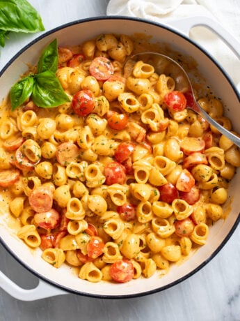 Cherry Tomato Pasta in a white skillet with a tomato cream sauce, herbs, and a spoon on the side.