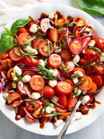 Tomato Salad in a white bowl with fresh basil, mozzarella, red onions, and balsamic glaze.