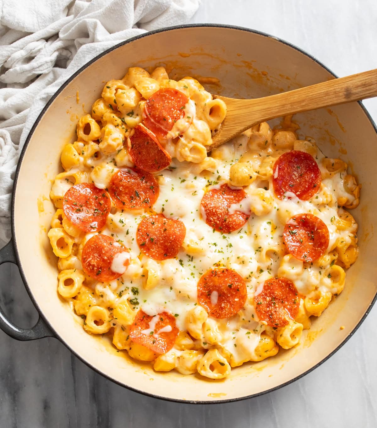 Pizza Mac and Cheese in a skillet with a wooden spoon on the side.