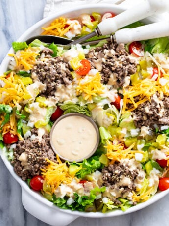 Big Mac Salad with big mac salad dressing, lettuce, ground beef, cheese, pickles, onions, and tomatoes in a white bowl.