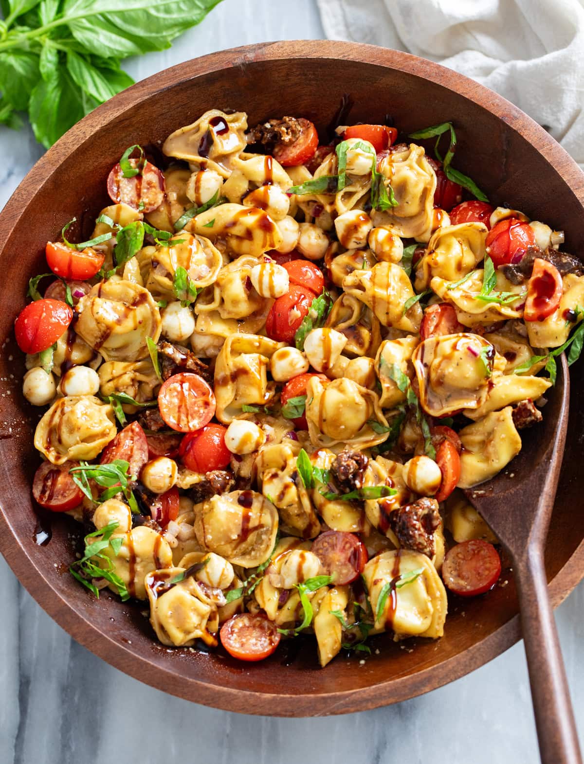 Caprese Pasta Salad in a wooden bowl with balsamic glaze drizzled on top.